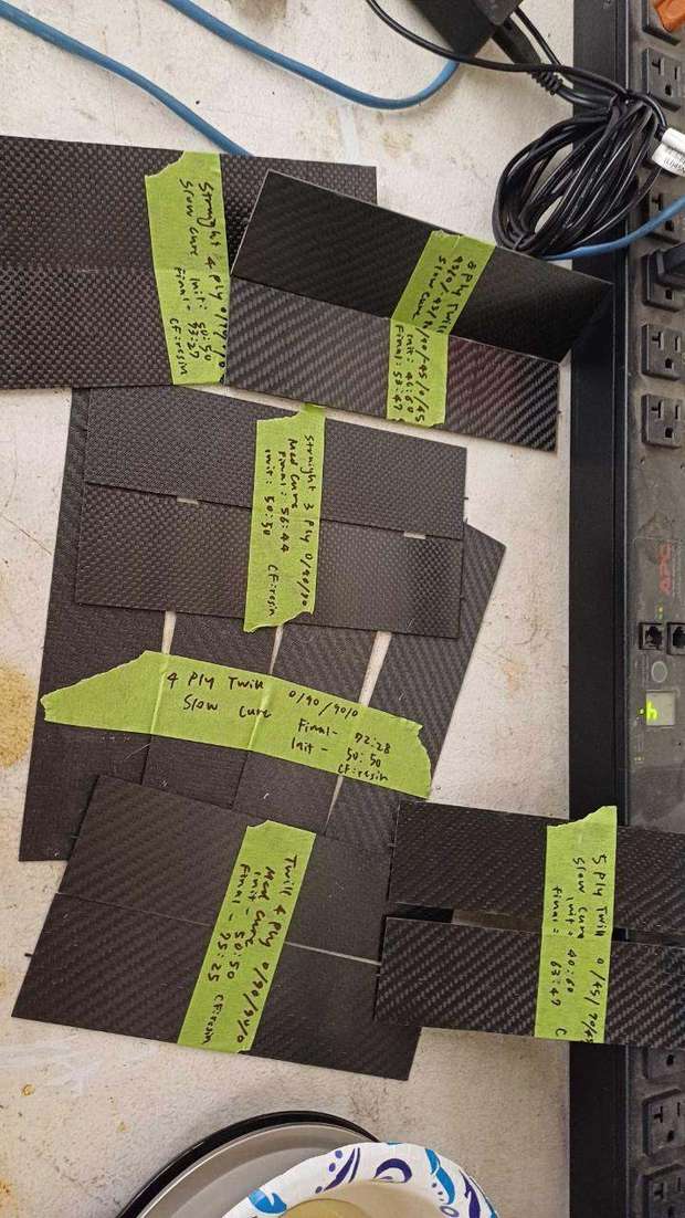 Carbon fiber test panels with handwritten labels listing layup and cure details